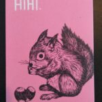 Eine rosarote Postkarte, auf der ein Eichhörnchen mit 2 Nüssen abgebildet ist. Oben links steht in weiß "HIHI.", unten rechts sind zwei Löcher in die Karte gestanzt worden.