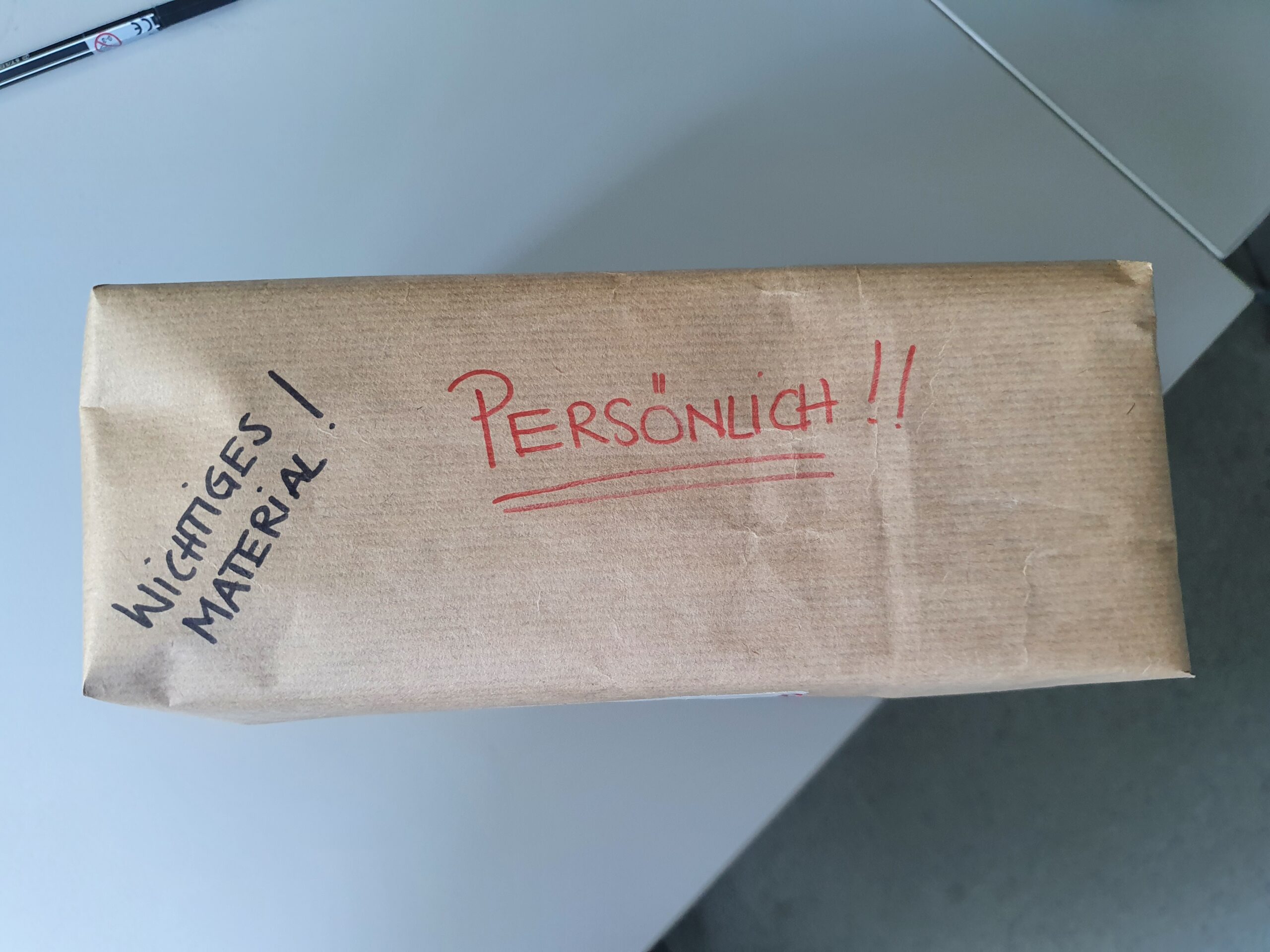 Ein braunes Paket mit roter und schwarzer Beschriftung: "Persönlich!", "Wichtiges Material!"